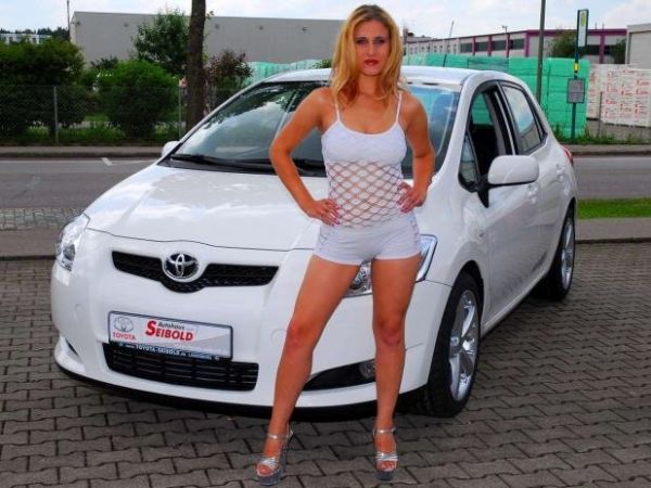 Blondes Girl in High Heels steht vor einem Toyota